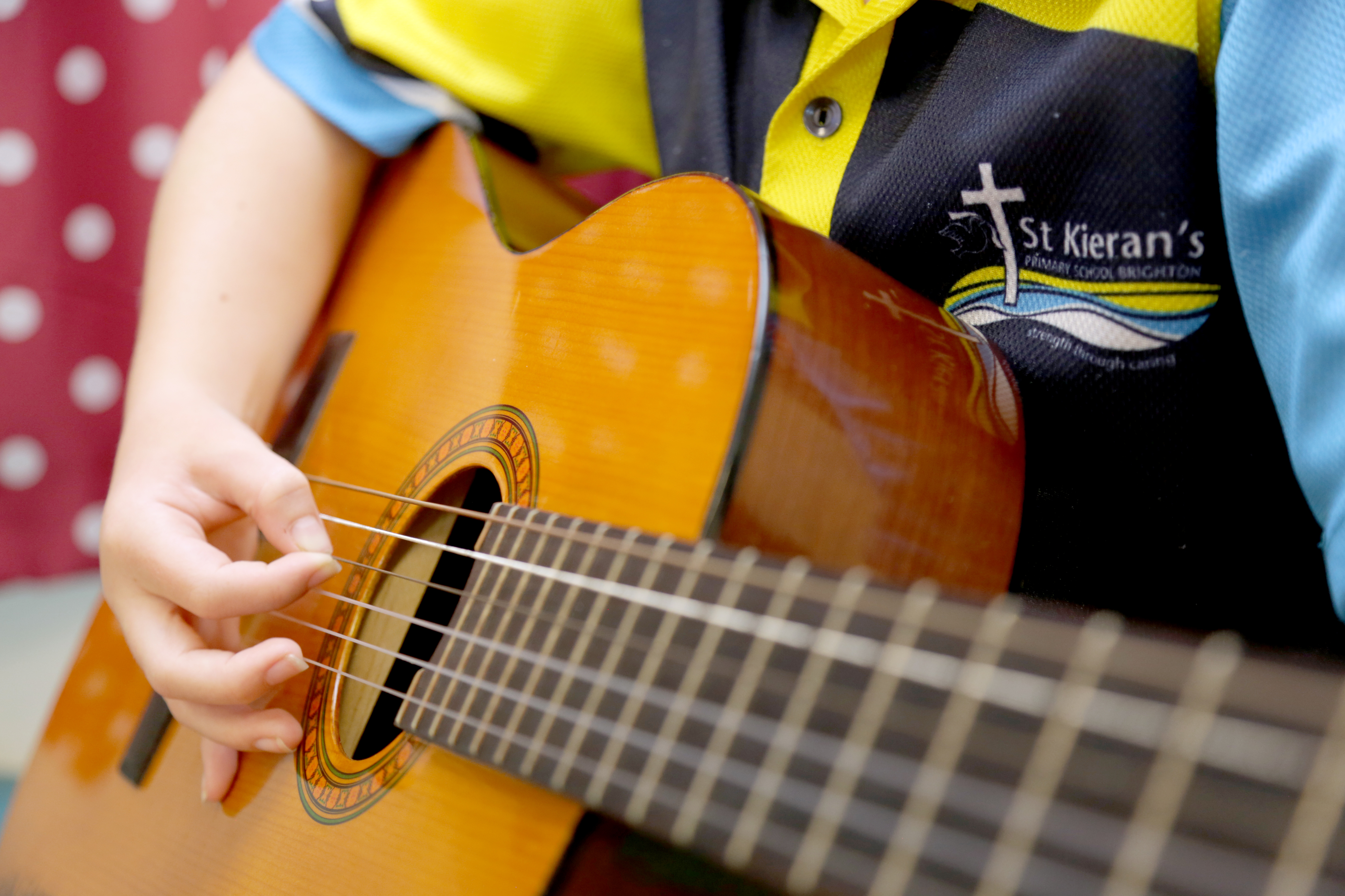 Student in school uniform playing an acoustic guitar during a music lesson